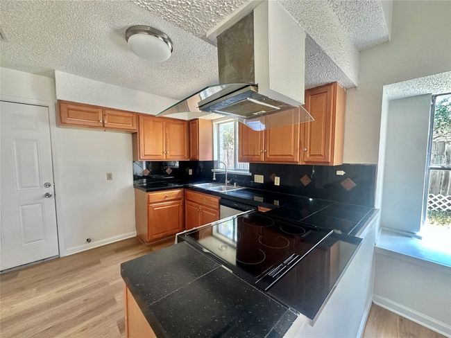 Kitchen with a peninsula, dark countertops, light wood-style flooring, brown cabinets, and a textured ceiling | Image 6