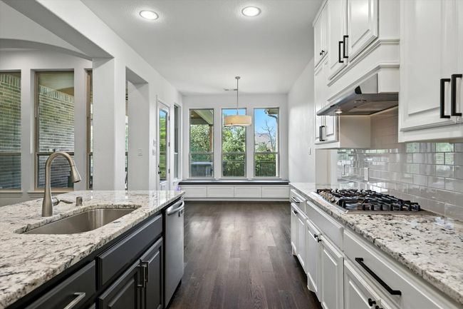 Kitchen with white cabinets, backsplash, dark wood finished floors, recessed lighting, and light stone counters | Image 13