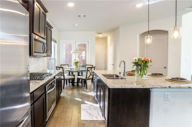 Kitchen featuring stainless steel appliances, backsplash, light wood-style flooring, dark brown cabinets, and pendant lighting | Image 12