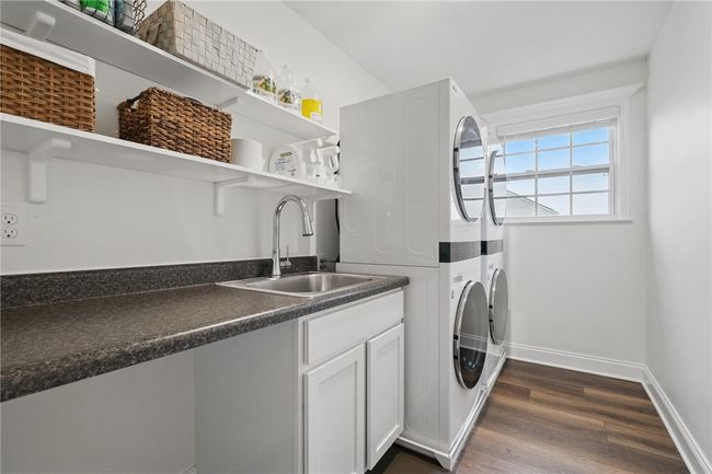 Well-appointed upper-level laundry room featuring two stacked washer and dryer units, a built-in utility sink, and generous counter space for folding. Open shelving offers convenient storage, while a large window brings in natural light to brighten the space. | Image 24