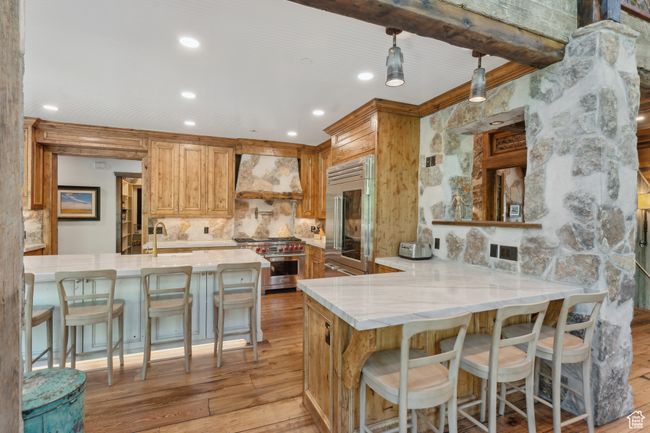 Kitchen with custom range hood, stainless steel appliances, light wood-type flooring, decorative backsplash, and light stone counters | Image 7