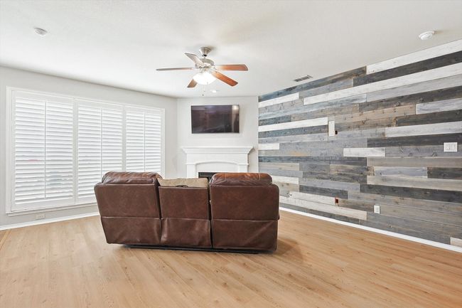 Living area with wooden walls, a ceiling fan, wood finished floors, a fireplace, and an accent wall | Image 8