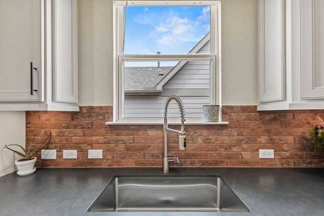 Kitchen with decorative backsplash, dark countertops, a sink, and white cabinetry | Image 11