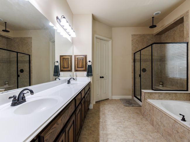 Dual vanities, a long mirror, a large walk-in shower with a rainfall showerhead, and tile flooring grace the primary bathroom. | Image 17