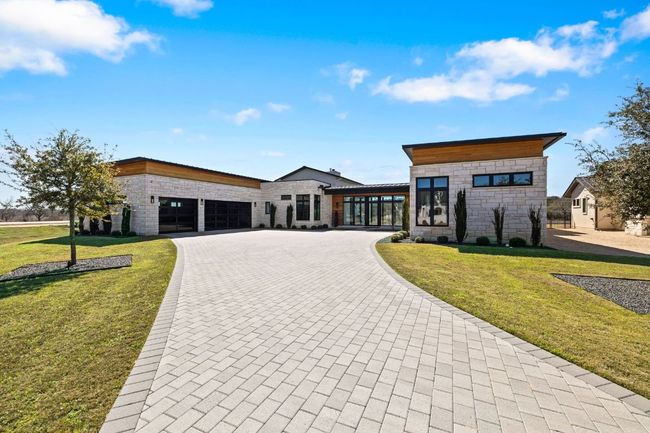 Contemporary house featuring a manicured front yard, stone siding, an attached garage, and curved driveway | Image 5