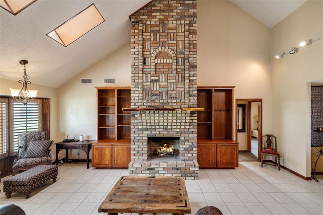 Living room with high vaulted ceiling, light tile patterned floors, a chandelier, a fireplace, and a skylight | Image 7