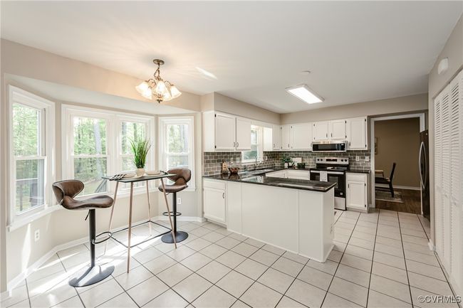 Kitchen with dark countertops, a sink, decorative backsplash, appliances with stainless steel finishes, and a notable chandelier | Image 22