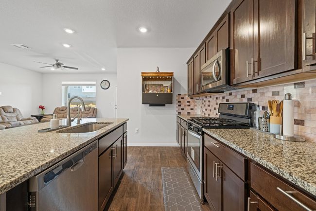 Kitchen with stainless steel appliances, a sink, a ceiling fan, light stone countertops, and dark wood-style flooring | Image 12