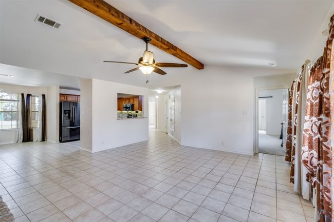 Unfurnished living room featuring lofted ceiling with beams, light tile patterned flooring, a ceiling fan, and visible vents | Image 7