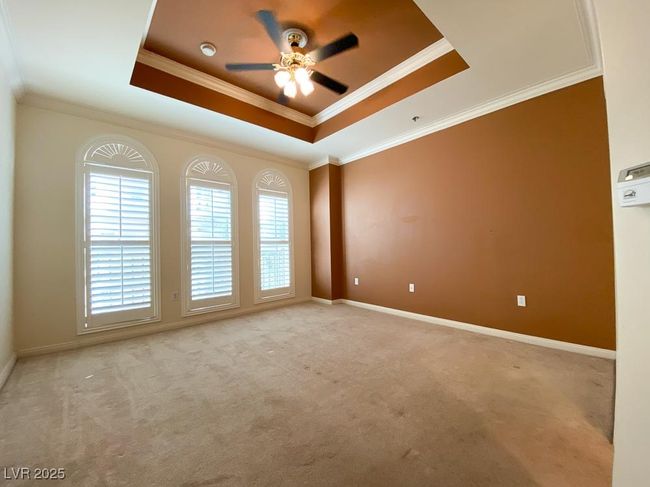 Empty room featuring a tray ceiling, a ceiling fan, carpet, and crown molding | Image 16