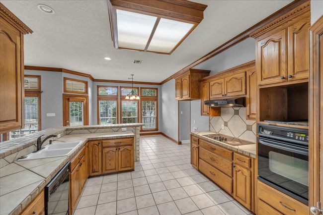 Kitchen featuring black appliances, decorative backsplash, brown cabinets, under cabinet range hood, and ornamental molding | Image 11
