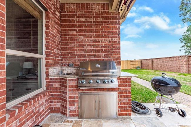 Brick outdoor kitchenette area with stainless steel grill, sink with granite counter tops. | Image 4