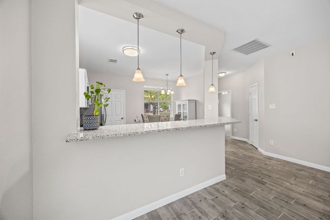 Kitchen with visible vents, a peninsula, baseboards, white cabinets, and wood finished floors | Image 13