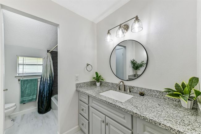 This bathroom features a modern design with a granite countertop, a stylish round mirror, and elegant lighting. | Image 29