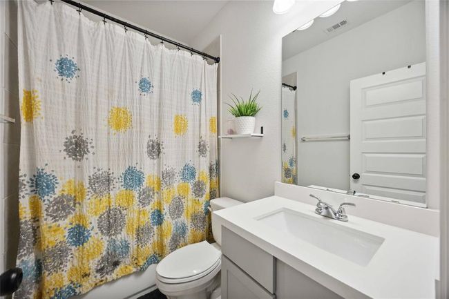 A modern bathroom featuring a clean white vanity with a polished sink, a large mirror, and a shower with a colorful, patterned curtain. The space is well-lit and includes a small shelf with a decorative plant for a touch of greenery. | Image 32