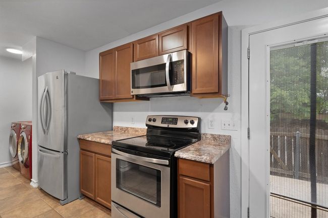 Kitchen featuring washing machine and dryer, stainless steel appliances, brown cabinets, light countertops, and light tile patterned flooring | Image 15