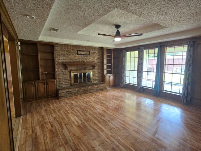 Unfurnished living room with built in features, a textured ceiling, ceiling fan, a raised ceiling, and wood finished floors | Image 6