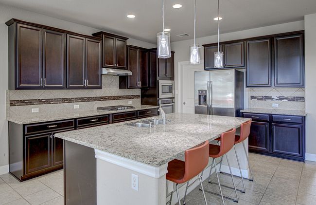 Kitchen featuring appliances with stainless steel finishes, light tile patterned flooring, a breakfast bar area, dark brown cabinetry, and an island with sink | Image 8