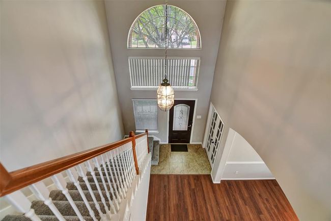 This inviting home features a spacious entryway with a high ceiling, elegant light fixture, and large arched window. The hardwood staircase with white railing complements the warm wood flooring, leading to a well-lit interior. | Image 41