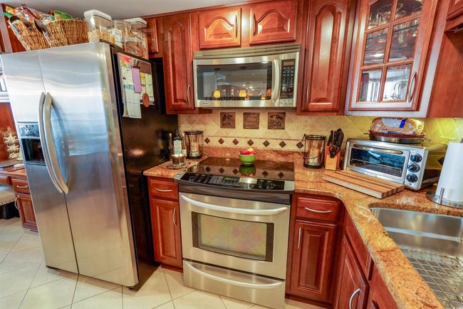 Kitchen with appliances with stainless steel finishes, light tile patterned floors, light stone countertops, backsplash, and dark brown cabinets | Image 18