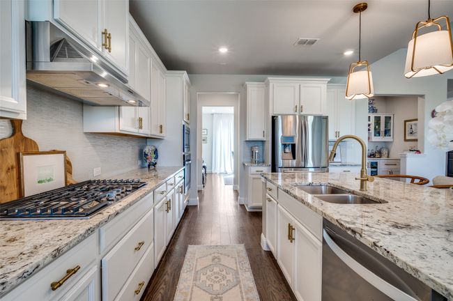 This kitchen boasts 5 burner gas cooktop, pot drawers, upgraded backsplash, white cabinetry, engineered wood flooring throughout and walk in pantry. | Image 11