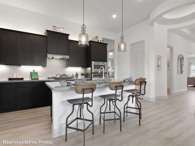 Kitchen with light wood-type flooring, backsplash, a kitchen island with sink, stainless steel appliances, and hanging light fixtures | Image 2