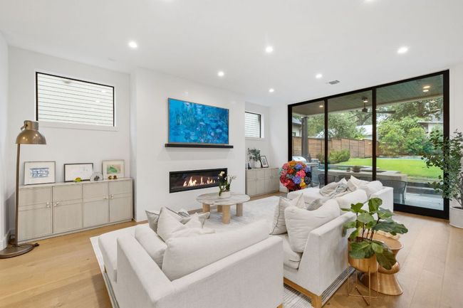 Living area with plenty of natural light, a wall of windows, light wood-style floors, recessed lighting, and a glass covered fireplace | Image 13