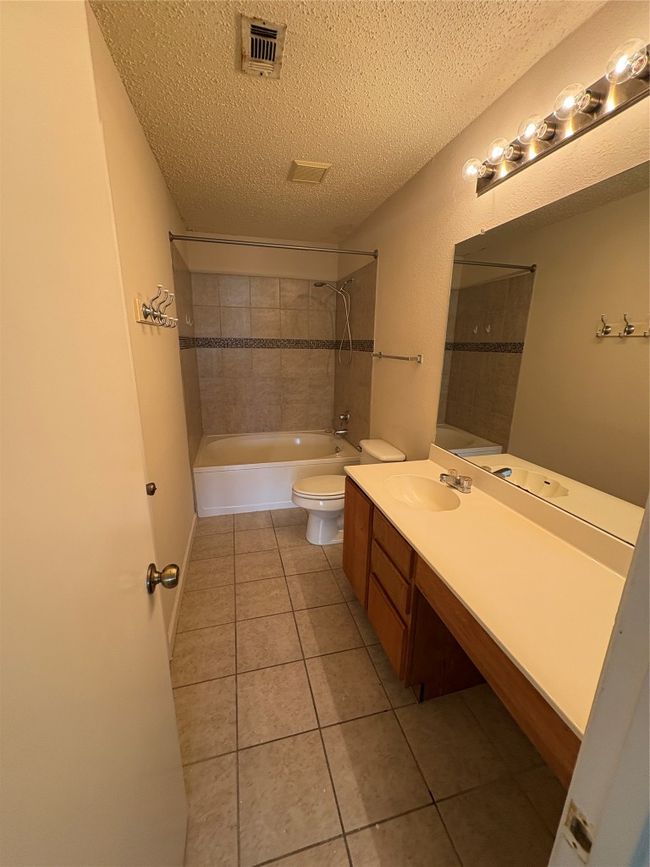Full bathroom featuring vanity, tile patterned floors, a textured ceiling, and washtub / shower combination | Image 12