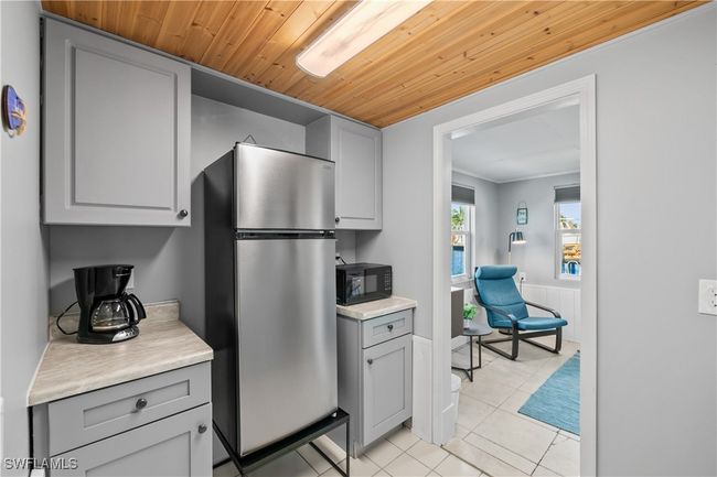 Kitchen with wooden ceiling, stainless steel refrigerator, light tile patterned floors, and gray cabinets | Image 31