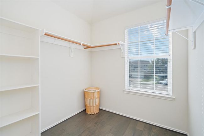 This photo shows a bright walk-in closet with ample shelving and hanging space, featuring a large window that lets in natural light. The space is well-organized and has a clean, modern look. | Image 30