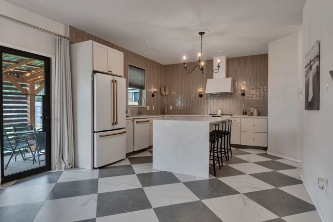 Kitchen with white appliances, a chandelier, white cabinetry, backsplash, and a center island | Image 12