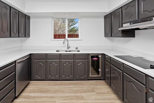 Kitchen with under cabinet range hood, a sink, black electric stovetop, beverage cooler, and stainless steel dishwasher | Image 9