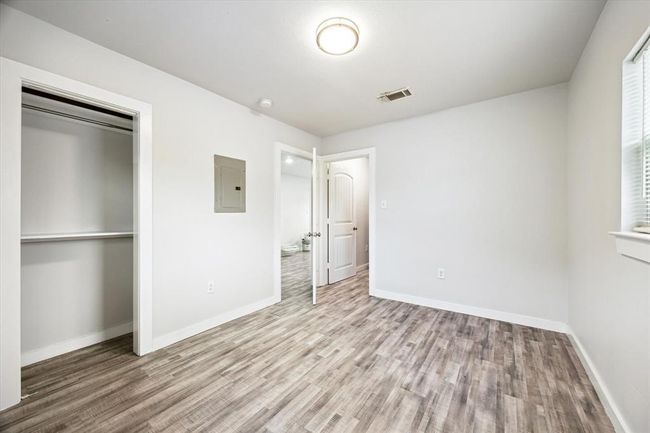 This is a bright, unfurnished room with light-colored walls and wood-look flooring. It features a closet with sliding doors, a window for natural light, and a modern ceiling light fixture. The room has a clean, neutral design, ready for personal touches. | Image 6