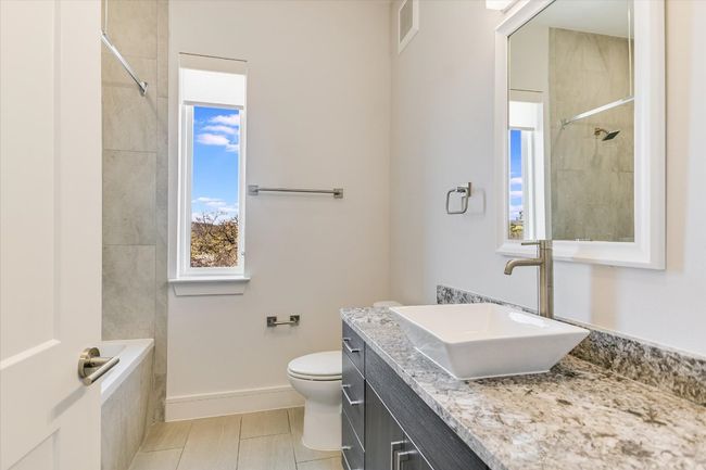 Bathroom with toilet, a tile shower, tile patterned flooring, baseboards, and vanity | Image 18