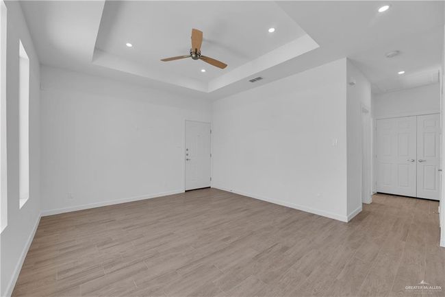 Empty room with a raised ceiling, ceiling fan, and light hardwood / wood-style flooring | Image 5