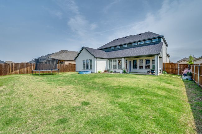 Rear view of property with a yard, a fenced backyard, a trampoline, and a shingled roof | Image 35