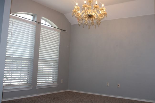 Carpeted empty room featuring a chandelier, baseboards, vaulted ceiling, and plenty of natural light | Image 6