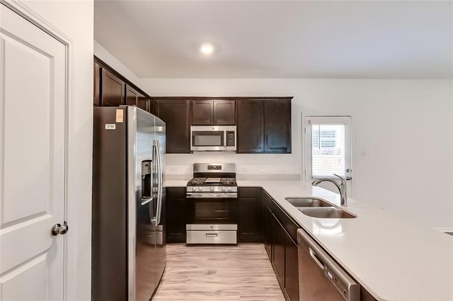 Kitchen featuring stainless steel appliances, a sink, dark brown cabinets, light wood-style flooring, and a peninsula | Image 11