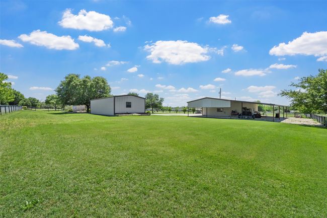 View of yard featuring a pole building, an outbuilding, a carport, and fence | Image 34