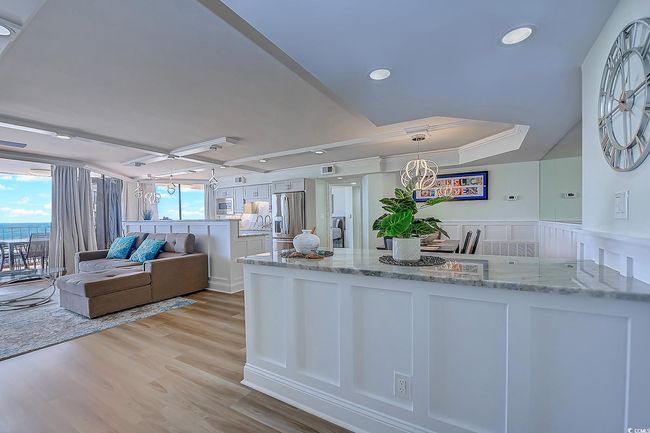 Kitchen with light wood-type flooring, decorative light fixtures, light stone counters, stainless steel refrigerator with ice dispenser, and a raised ceiling | Image 6