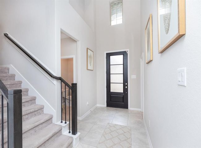 welcoming entryway with high ceilings, a modern black front door with frosted glass, and light tiled flooring. | Image 6