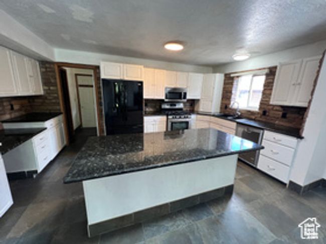 Kitchen with appliances with stainless steel finishes, white cabinetry, a center island, dark stone counters, and baseboards | Image 4