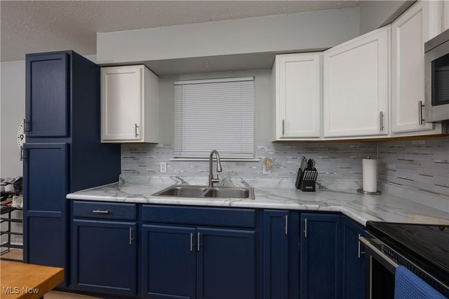 Kitchen featuring blue cabinetry, stainless steel microwave, decorative backsplash, and white cabinets | Image 9