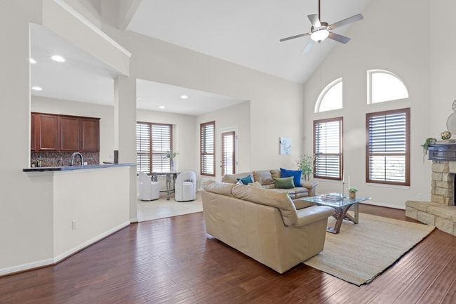 Living area featuring ceiling fan, a stone fireplace, recessed lighting, wood finished floors, and high vaulted ceiling | Image 7