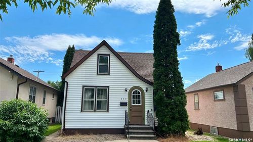 White siding exterior featuring a brown arched entry door, dark trim windows, and a peaked roofline | Card Image
