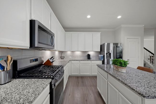 Kitchen featuring decorative backsplash, light wood-style flooring, ornamental molding, stainless steel appliances, and a kitchen island | Image 6