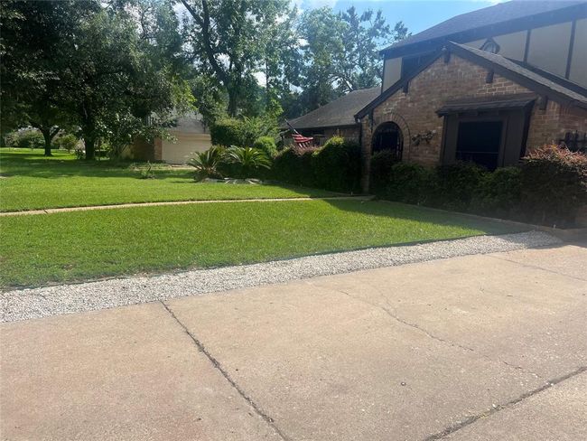 Charming brick home with a lush, green front lawn and mature trees. The driveway has a gravel border, and the house features large windows and a well-maintained garden. Peaceful suburban setting. | Image 4