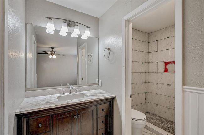 Bathroom featuring toilet, vanity, ceiling fan, tiled shower, and a textured wall | Image 20