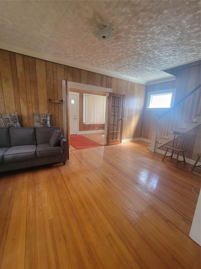 Unfurnished living room featuring baseboards, a textured ceiling, wood walls, and light wood-style floors | Image 6