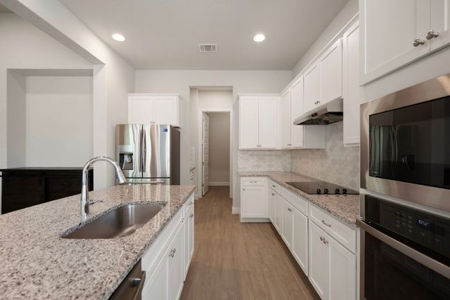 Kitchen with appliances with stainless steel finishes, a sink, under cabinet range hood, light wood-type flooring, and white cabinets | Image 7